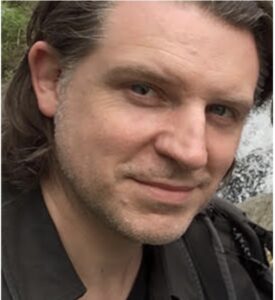 A dark haired scruffy faced gentleman ... no. A dark haired scruffy faced man who might just be roguish is inviting you on an adventure with a raised eyebrow and tilt of the head.
