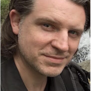 A dark haired scruffy faced gentleman ... no. A dark haired scruffy faced man who might just be roguish is inviting you on an adventure with a raised eyebrow and tilt of the head.