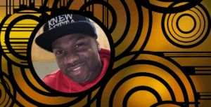 Knewbetta's warm smile invites us into the world of story. He's a man of African ancestry wearing a bright red cozy sweatshirt and a jaunty black baseball cap. He's standing in his kitchen with a gentle tilt of his head like he's welcoming us to sit down, kick up our feet, and listen to a great story.