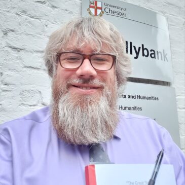 Brenton Dickieson smiles and squints into the light. He is a man of European descent with a flowing reddish beard.