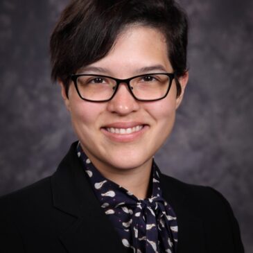 Robbie Park is looking us squarely in the eye with a broad grin as though this is about to turn into a wild adventure! her dark hair is swept to the side, she has dressed professionally for this photo, and she must have amazing stories to tell!