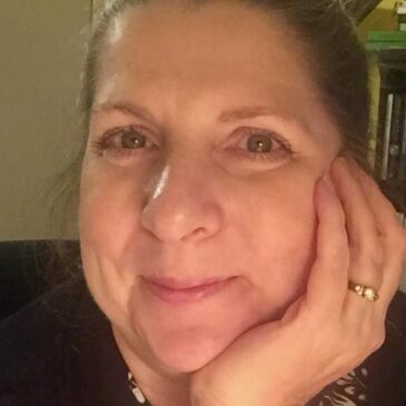 Kris Swank can barely hold in her bubbling laughter. She is clearly amused at this opportunity to share her image. She's leaning her chin on her beringed left hand and her green eyes and deep dimples remind us: Librarians Have More Fun.