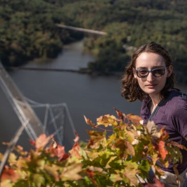 A vibrant woman with glasses and brown hair outdoors in the autumn foliage