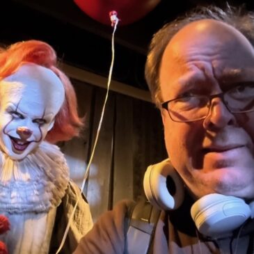 A gentleman of European extraction wearing headphones around his neck is looking over his spectacles at a truly terrifying clown doll. there's a bloon. I can't even keep alt-texting, the clown is so disturbing.