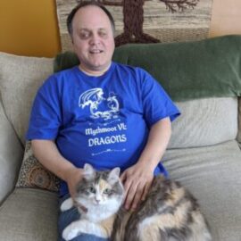 Christopher holding a girl cat and wearing the Mythmoot Dragons shirt